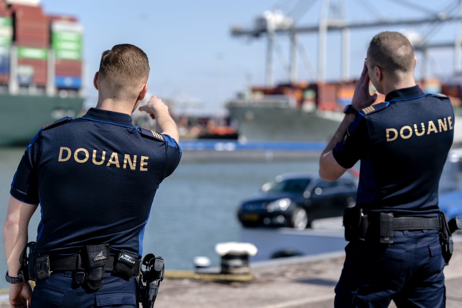 Twee douaniers kijken met een verrekijker richting de haven.