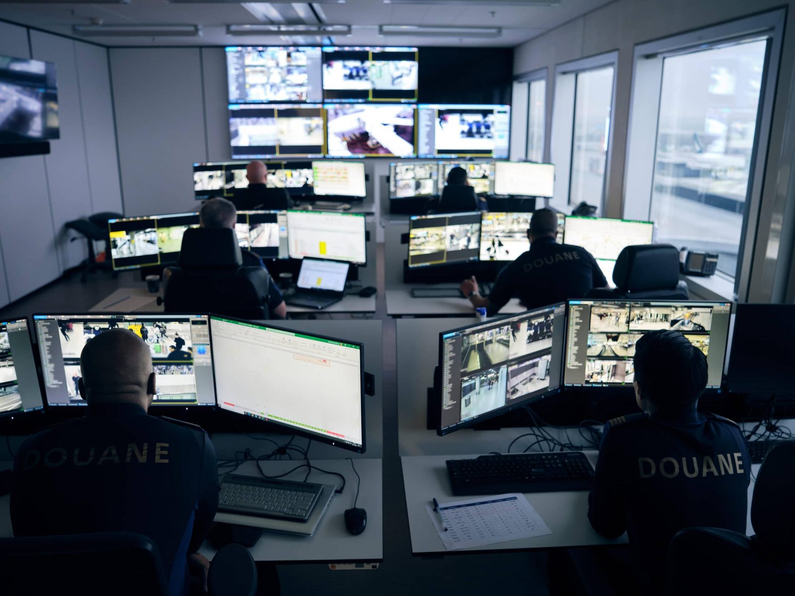 Een ruimte met douaniers die op computerschermen naar camerabeelden kijken