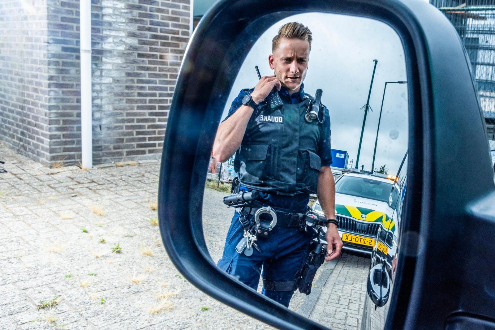 Een medewerker van de Douane in het uniform van Fysiek Toezicht (FT) met handboeien, portofoon en een wapen. 