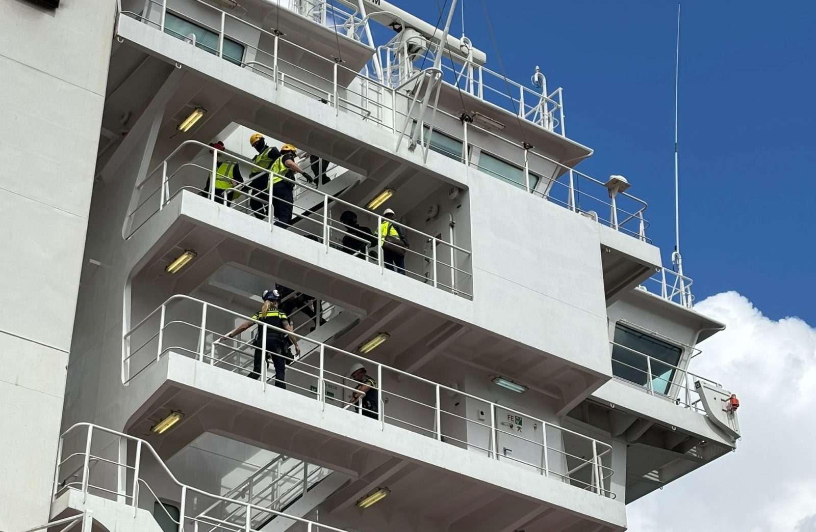 Douanemedewerkers aan boord van een containerschip lopen de trappen af aan de buitenzijde van de commandobrug.