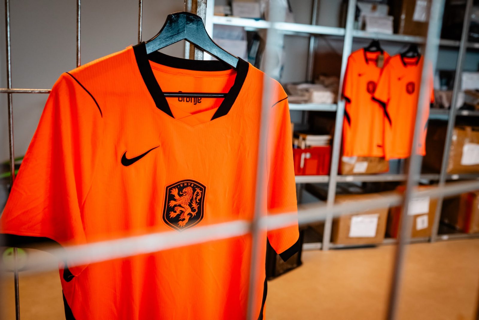 Namaak Oranjeshirts afgesloten achter een hek van de opslag op Schiphol. 